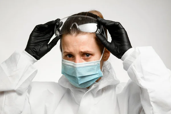 Молодая медсестра в медицинской маске держит руки на защитных очках к голове — стоковое фото