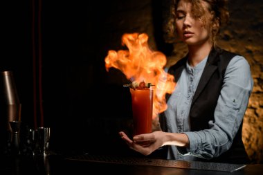 Profesyonel kadın barmen bardağını kokteyl ile tutar ve ustaca yakar.