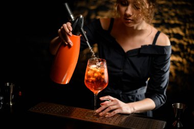 Kadın barmen portakal suyu bardaktan bardağa parlak içecekle doldurur.