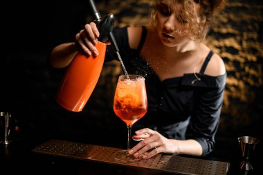 Kadın barmen dikkatli bir şekilde portakal sifonundan bardağa parlak içecekle sıvı dök.