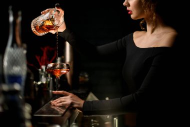 Profesyonel kadın barmen ustalıkla bardağa içki doldurur.