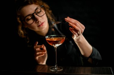 Yakın plan. Genç bayan barmen içkiyle bardağa malzeme ekliyor.