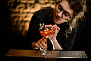 Güzel genç bir barmen, cımbız kullanarak dikkatle bir bardak içki süslüyor.