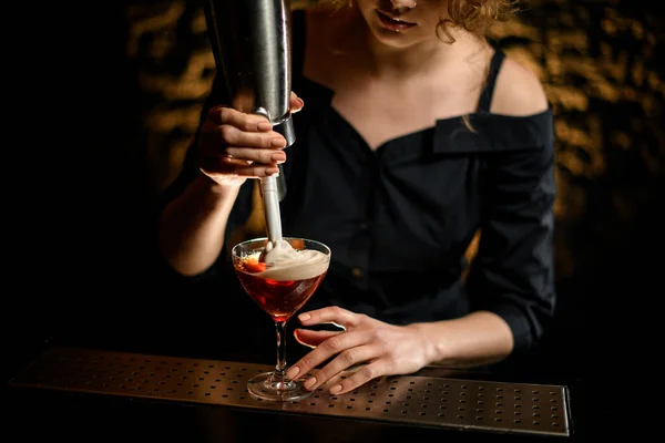 Vrouwelijke barman voegt schuim toe aan glas met cocktail. — Stockfoto