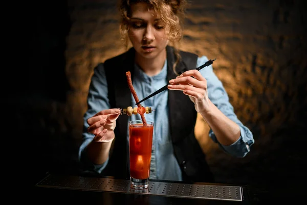 woman bartender neatly decorates glass with ready-made Bloody Mary cocktail