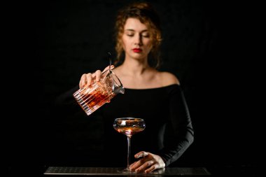 Karanlık odadaki seksi barmen kız bardağa dolduruyor.