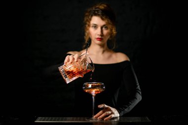 Karanlık odadaki güzel barmen kız bardağa kokteyl dolduruyor.