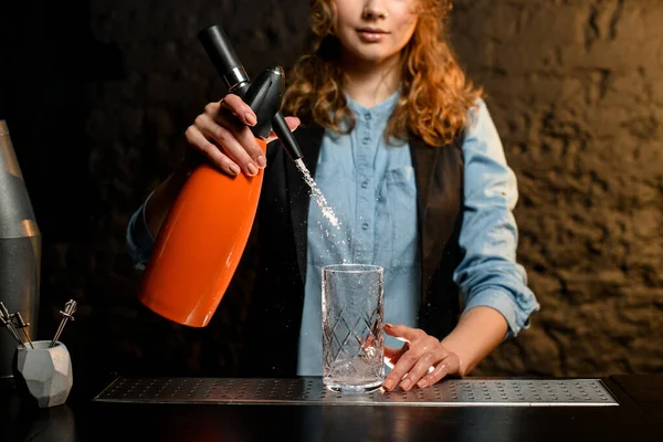 Garçom menina segura sifão laranja e derrama água a partir dele — Fotografia de Stock