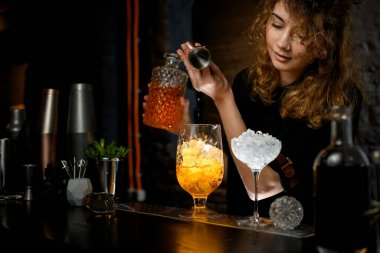 Kadın barmen jigger 'dan bardağa buz doldurur..