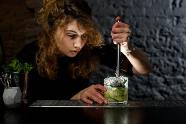 Kadın barmen alkollü kokteyl yapıyor ve bardağa meyve suyu sıkıyor.