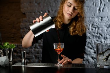 Genç bayan barmen bardağa çelik bardaktan kokteyl dolduruyor.