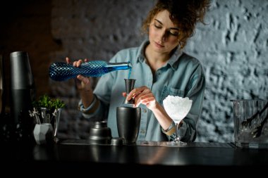 Kadın barmen şişeden jigger 'a mavi likör dolduruyor..