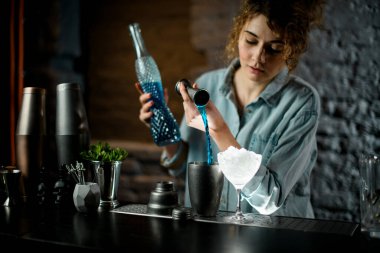 Profesyonel bayan barmen jigger 'dan bardağa mavi içki doldurur..