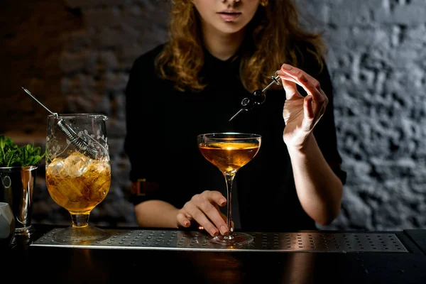 Menina no bar segura pequena espada com cerejas sobre vidro com coquetel — Fotografia de Stock