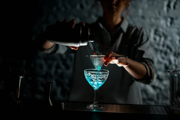 Chica en la barra oscura vierte la bebida azul brillante de agitador en vidrio —  Fotos de Stock