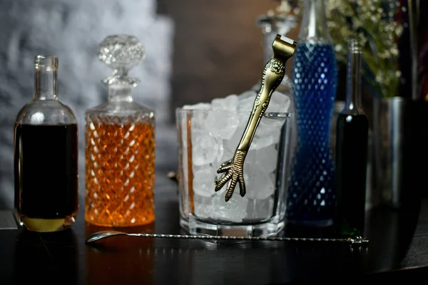 Varias botellas de bebida y vidrio con trozos de hielo y pinzas de metal en el mostrador de la barra . — Foto de Stock