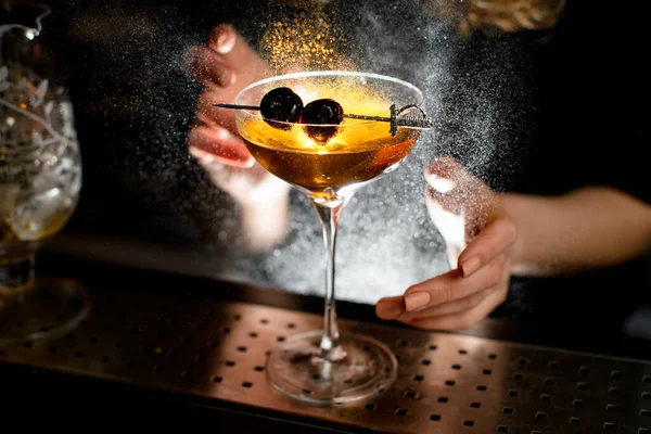 Gros plan. Barman saupoudrer sur verre avec un cocktail qui a décoré petite épée avec des cerises — Photo