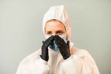 Yüzündeki cerrahi maskeyi düzelten kapüşonlu beyaz giysili genç doktor portresi..