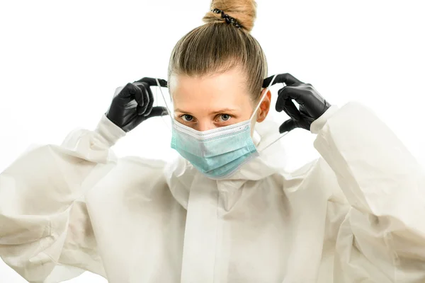 Блондинка в белом защитном костюме и черных перчатках надевает хирургическую маску — стоковое фото
