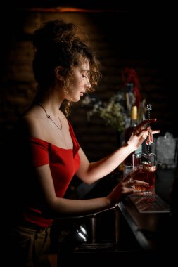 Karanlık bardaki genç bayan bardakta kaşık ile içki karıştırıyor.
