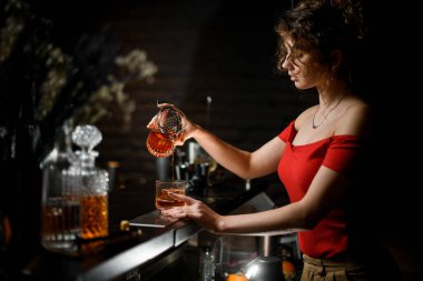 Çekici kadın barmen kadehten bardağa kokteyl doldurur.