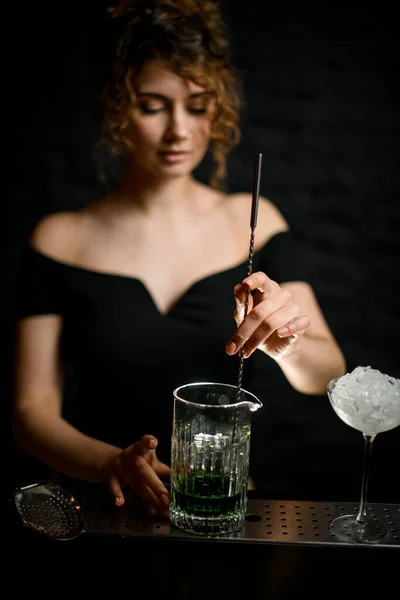 Close-up. Young handsome female barman stirring drink in cup with bar spoon — Stock Photo, Image