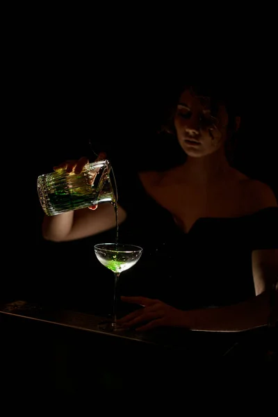 Atraktivní žena barman v tmavém baru nalévá koktejl z poháru na sklo — Stock fotografie