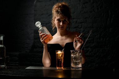 Genç çekici bayan barmen elinde sürahi ve elinde metal jigger tutuyor.