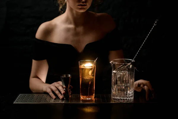 Vaso con bebida alcohólica brillante, taza de mezcla con cuchara y soporte de jigger de metal en el mostrador de bar . — Foto de Stock