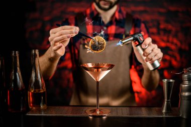 Erkek barmen kokteyli martini bardağıyla süsleyip ateşe veriyor.