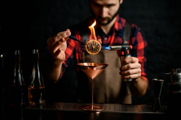 Barman macho sostiene pinzas con rodajas de cítricos y le prende fuego — Foto de Stock