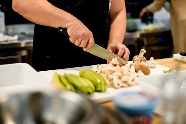 Szef kuchni tnie zielone cukinie i grzyby champignon z nożem na kawałki. — Zdjęcie stockowe