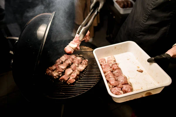 男性料理人はバーベキューグリルに生肉をトングで丁寧に広げ — ストック写真