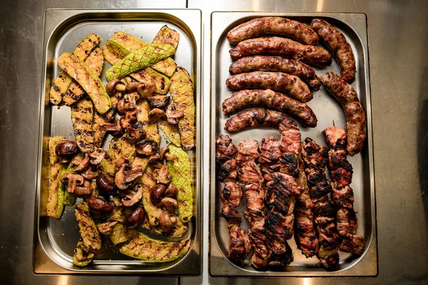 肉、ソーセージ、野菜、キノコをグリルした2つの金属トレイのトップビュー — ストック写真