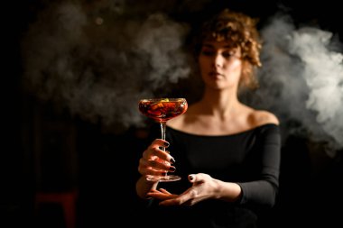 Genç ve güzel bir kadın bardağı önünde kokteyl ile tutuyor..