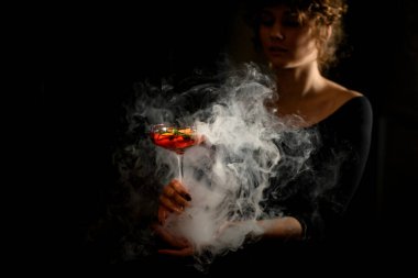 Genç ve güzel bir kadın bardağı önünde parlak bir kokteyl ile tutuyor..