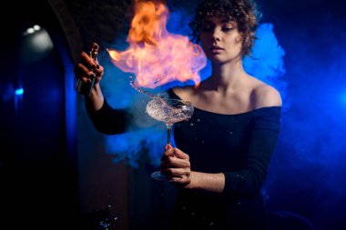 Güzel bayan barmen bardağı bardakla su sıçratır, serper ve üzerine ateş yakar..