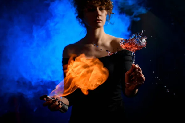 Mujer bonita con atención sostiene el vidrio con salpicadura de bebida, rocía y prende fuego a ella . — Foto de Stock