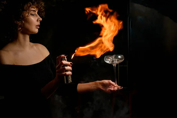 Hermosa mujer sostiene vidrio con salpicaduras de cóctel alcohólico aspersiones y hacer fuego en ella . — Foto de Stock