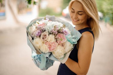 Genç, güzel, gülümseyen sarışın kadın elinde buketi tutuyor ve ona bakıyor.