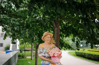Neşeli, gülümseyen, şapkalı, pembe çiçekli, yuvarlak kutulu sarışın kız.