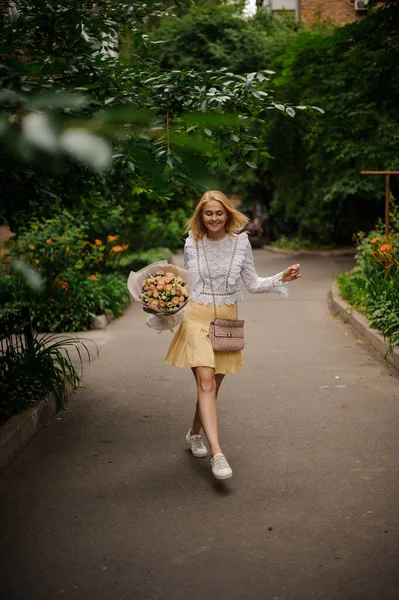 Молода усміхнена жінка ходить в парку з букетом троянд в руці . — стокове фото