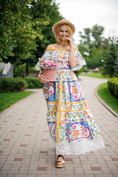 Schöne blonde Frau mit rosa Blumenkasten spaziert durch den Park — Stockfoto