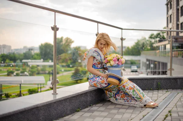 예쁜 소녀가 둥근 꽃 상자를 들고 발코니에 앉아 있다. — 스톡 사진