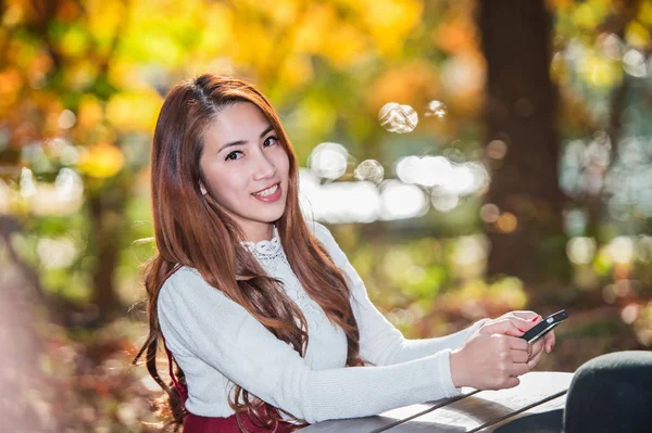 Mulher bonita sorrindo e mão segurando smartphone no outono . Fotos De Bancos De Imagens