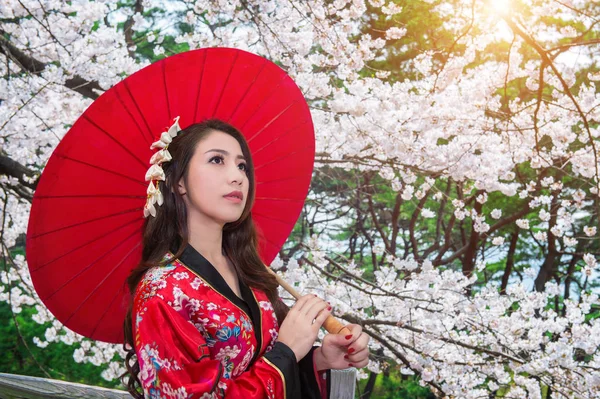 Asian woman wearing traditional japanese kimono with red umbrella and cherry blossom. — Stock Photo, Image