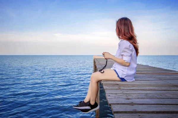Chica sentada sola en un puente de madera en el mar. Estilo de tono vintage . —  Fotos de Stock