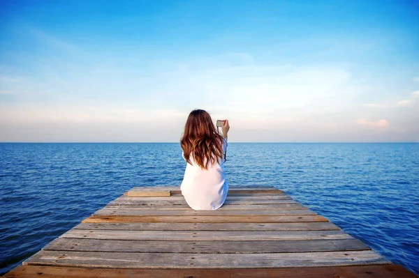 여자 혼자 앉아 및 손 카메라를 들고는 바다에 목조 다리. — 스톡 사진