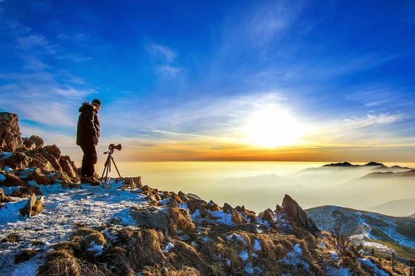 Fotógrafo profesional toma fotos con cámara en trípode en pico rocoso al atardecer . — Foto de Stock