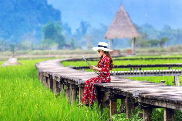 Jovem mulher sentada no caminho de madeira com campo de arroz verde em Vang Vieng, Laos . — Fotografia de Stock